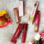 Produtos de beleza, incluindo batom e balm labial, dispostos sobre uma pelagem branca e macia.