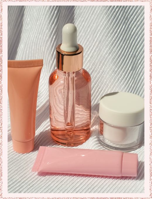 Frascos de cosméticos: um frasco rosa, um tubo de creme e um tubo de bálsamo labial sobre fundo neutro.