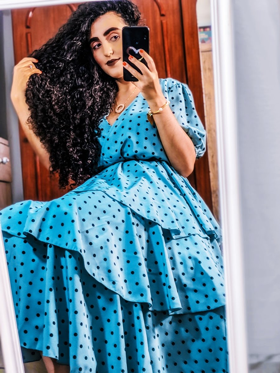 Mulher vestindo um vestido azul de bolinhas tirando uma selfie, sorrindo e capturando um momento descontraído.